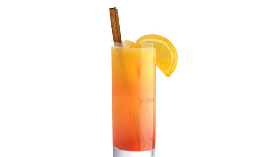 A Tom Collins glass containing orange spice punch garnished with a stick of cinnamon